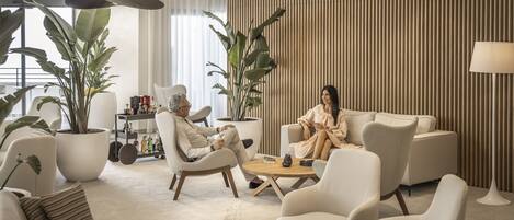 A modern living room with a sofa, armchairs, and a coffee table. There are potted plants and a lamp.