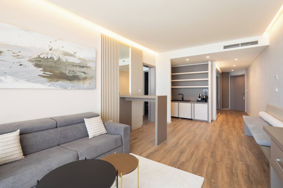 Een moderne woonkamer met een grijze bank, een ronde salontafel en een groot abstract schilderij aan de muur.