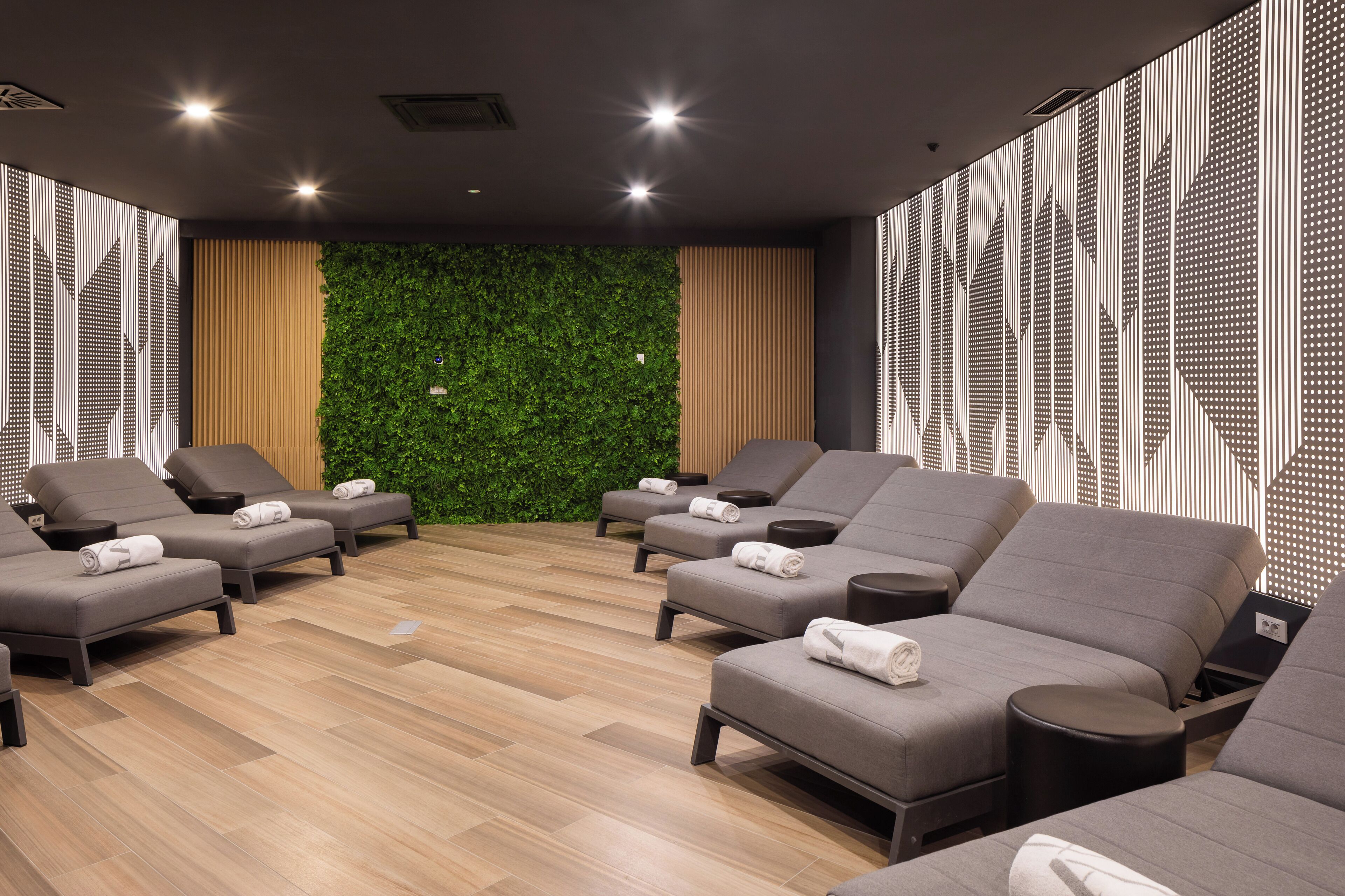 A spa room with multiple grey lounge chairs, a green wall, and a patterned wall design.