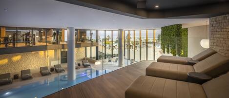 Un espace piscine intérieur moderne, doté de coins détente et d’équipements de musculation.