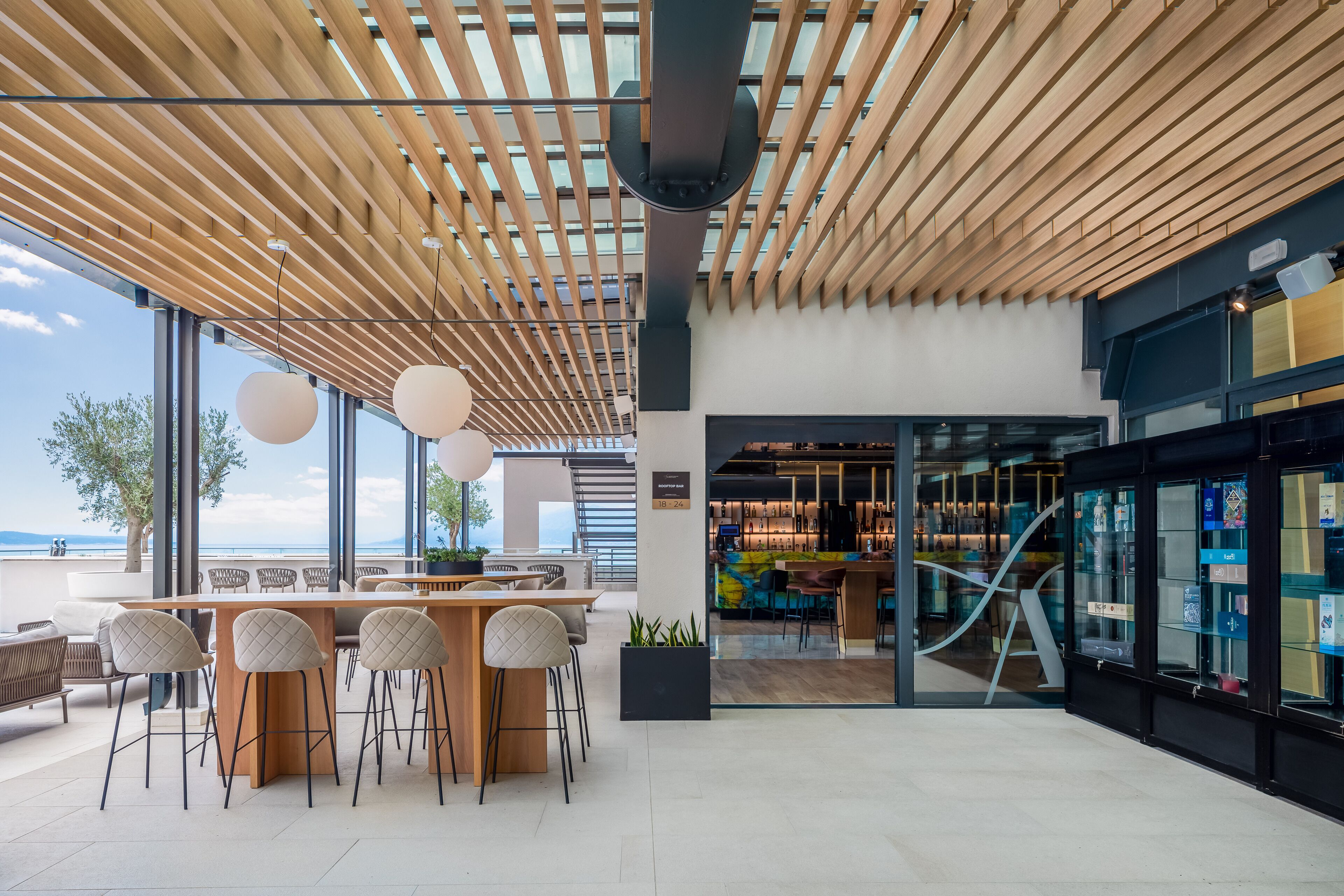 A modern bar area with a wooden ceiling, large windows, and a view of the sea.