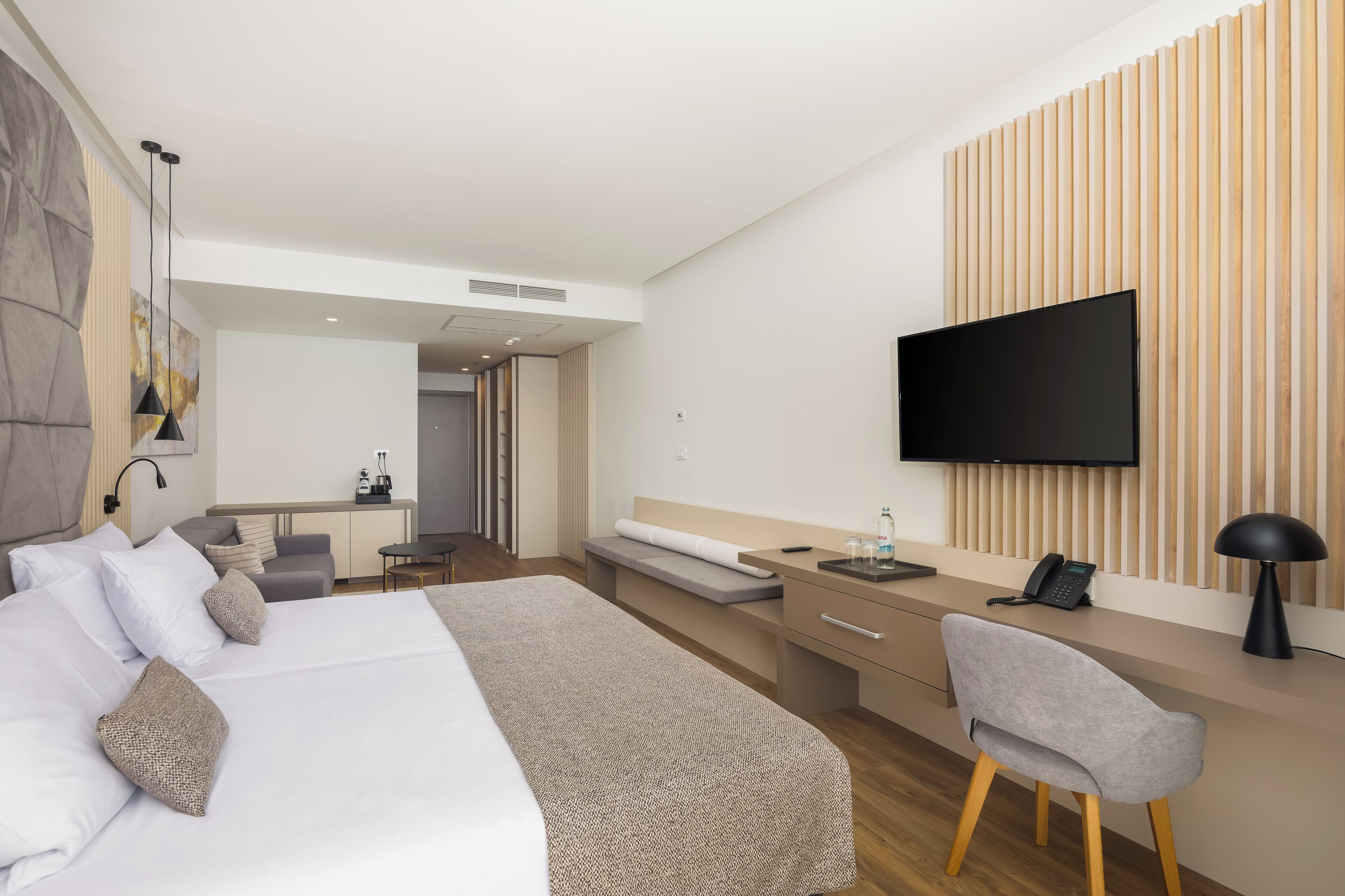 Et moderne hotelværelse med en stor seng, et skrivebord med stol, et fladskærms-tv og en væg med trælameller.