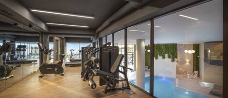 Un gimnasio moderno con equipo de ejercicio, ventanas amplias y vista a una zona de piscina.