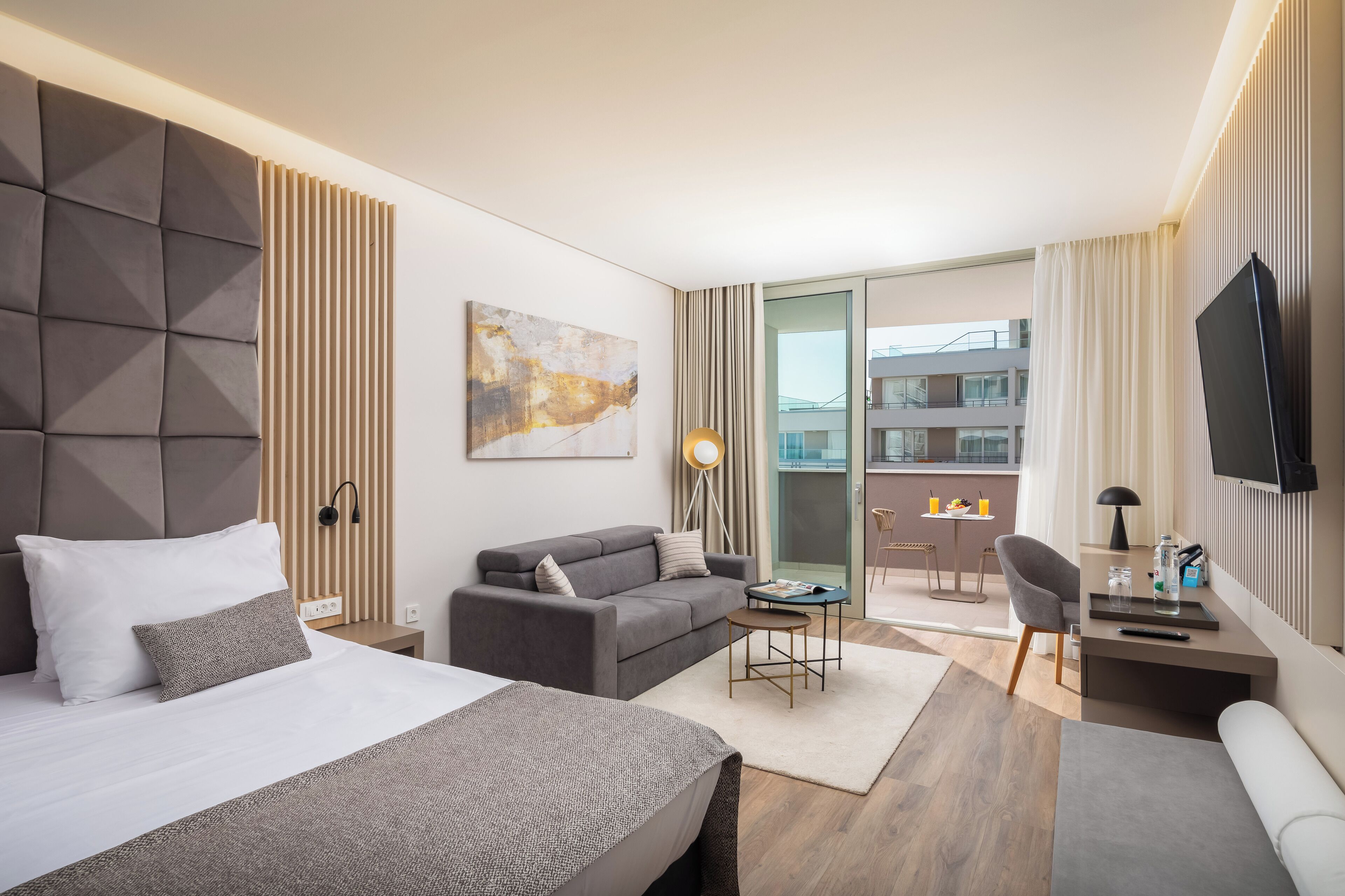 Ett modernt hotellrum med en stor säng, en soffa, ett litet bord och en tv.
