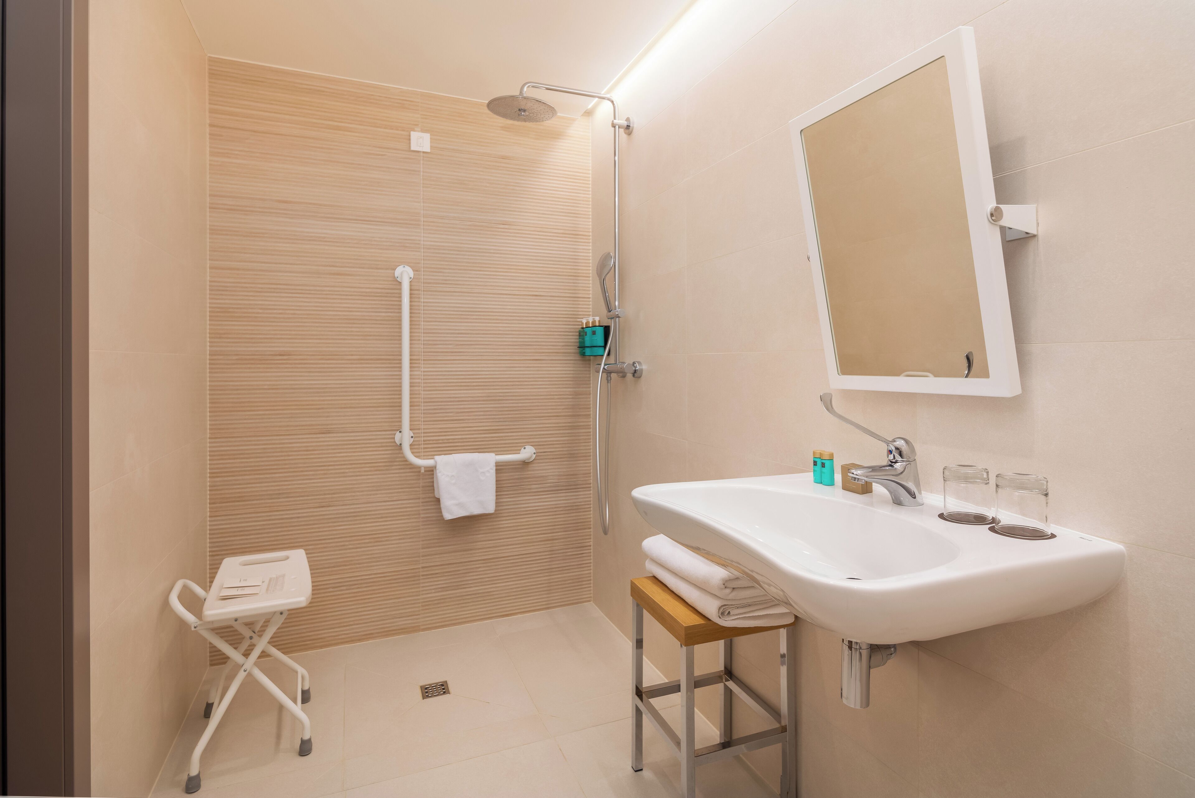 Un baño moderno con ducha, un lavamanos con dos vasos y un perchero para toallas.