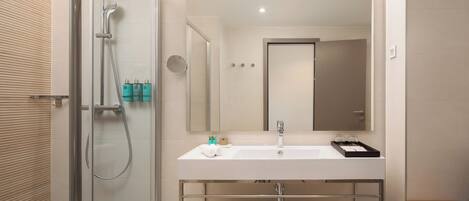 A modern bathroom with a glass-enclosed shower, a white sink with a mirror above it, and neatly folded towels on a shelf.