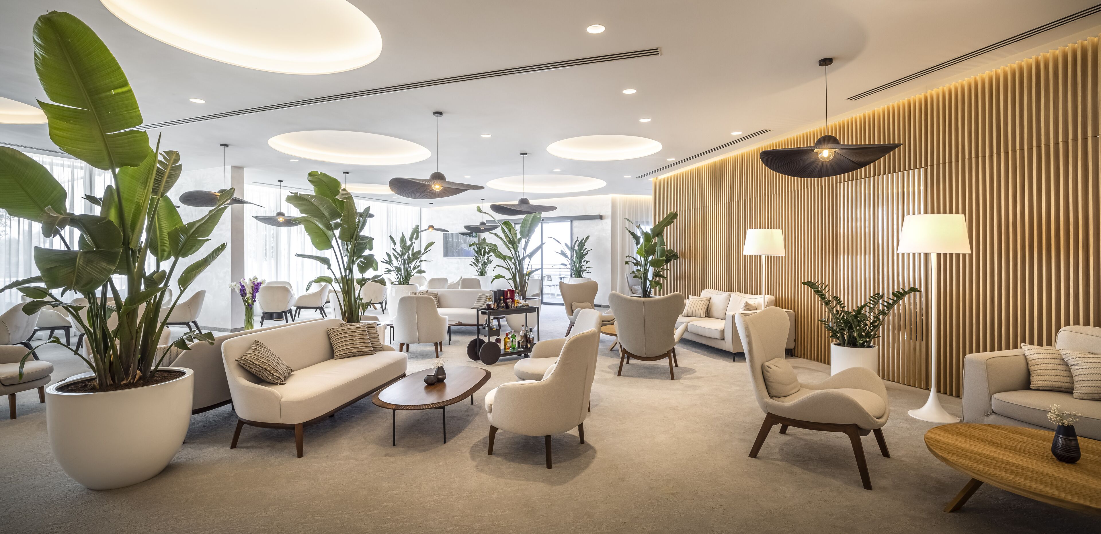 Un hall d’hôtel moderne avec un espace salon central, de grandes plantes en pot et un mur décoratif en bois.