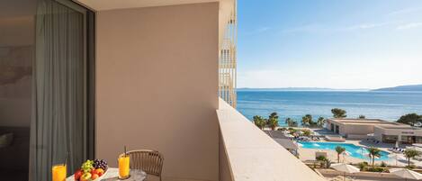 A balcony with a table set with fruit and drinks, overlooking a pool and ocean.