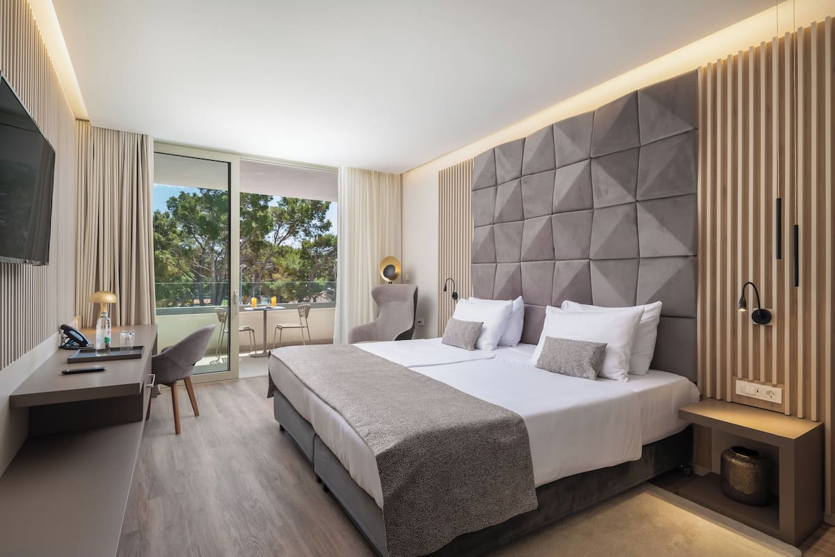 Een moderne hotelkamer met een groot bed, een bureau met stoel, een televisie en uitzicht op het omliggende landschap.