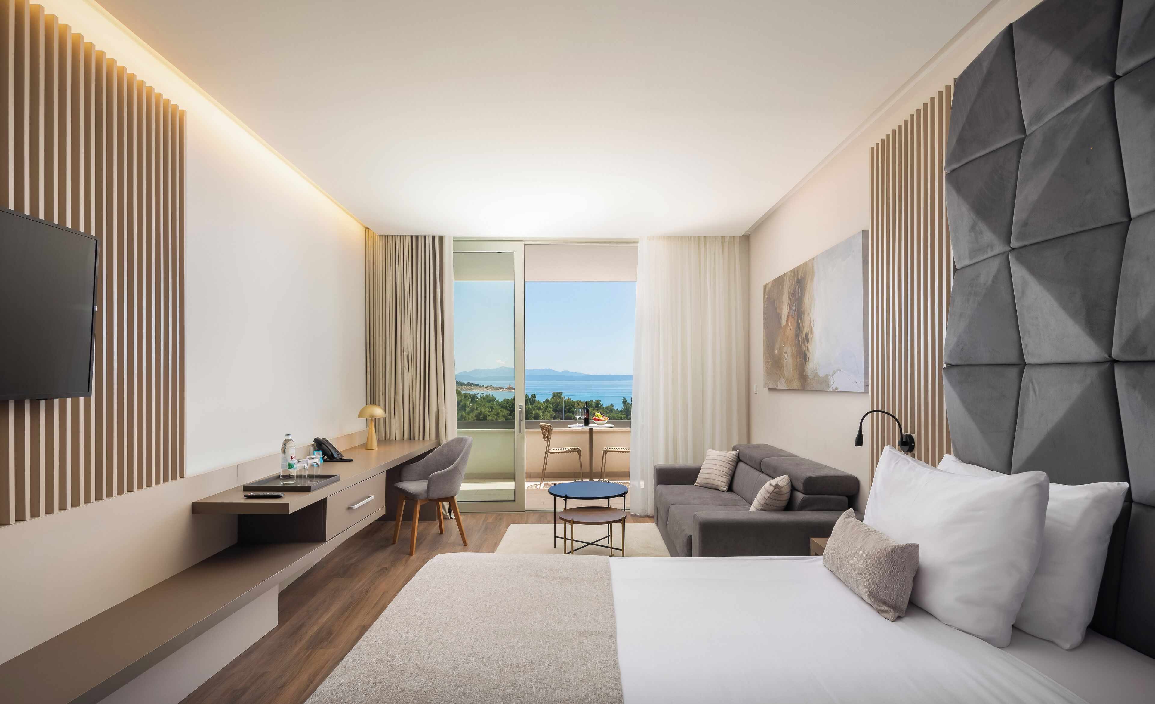 Een moderne hotelkamer met een groot bed, een bureau, een bank en een balkon met uitzicht op zee.
