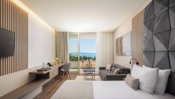 Een moderne hotelkamer met een groot bed, een bureau, een bank en een balkon met uitzicht op zee.