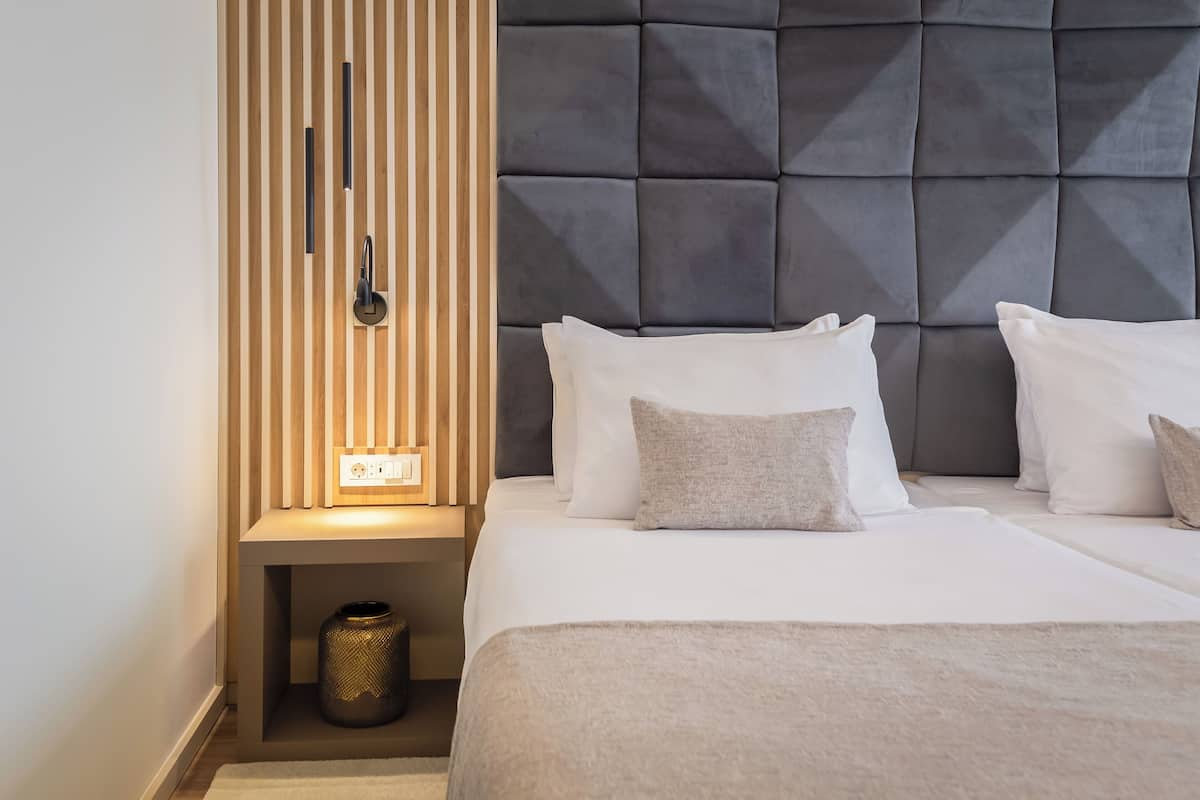 Een moderne hotelkamer met een gestoffeerd hoofdeinde, een nachtkastje met een lamp en een kleine decoratieve vaas.