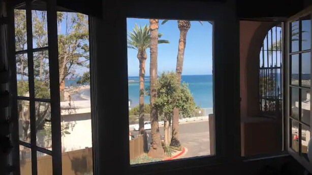 A room with a view of palm trees and the ocean through large windows. - Stylish Beachside. Parking.Views. FrontofBdg. (San Pedro)