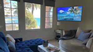 A living room with a blue sofa, a grey sofa, a white coffee table, and a TV displaying a tropical beach scene. - Stylish Beachside. Parking.Views. FrontofBdg. (San Pedro)