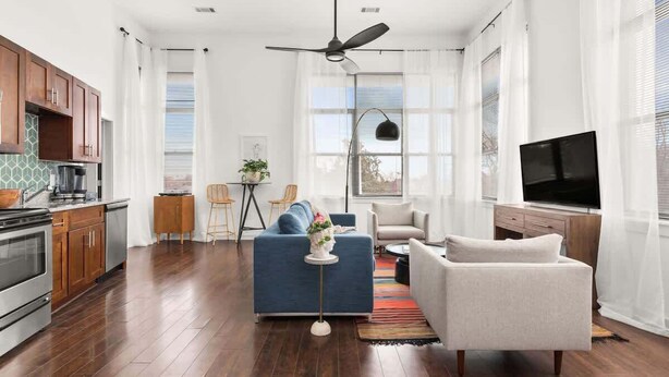 A modern living room with a blue sofa, a white armchair, a TV, and a ceiling fan.