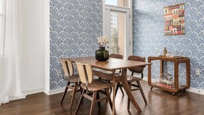 A dining area with a wooden table, four chairs, a vase, and a small side table with a decorative item.