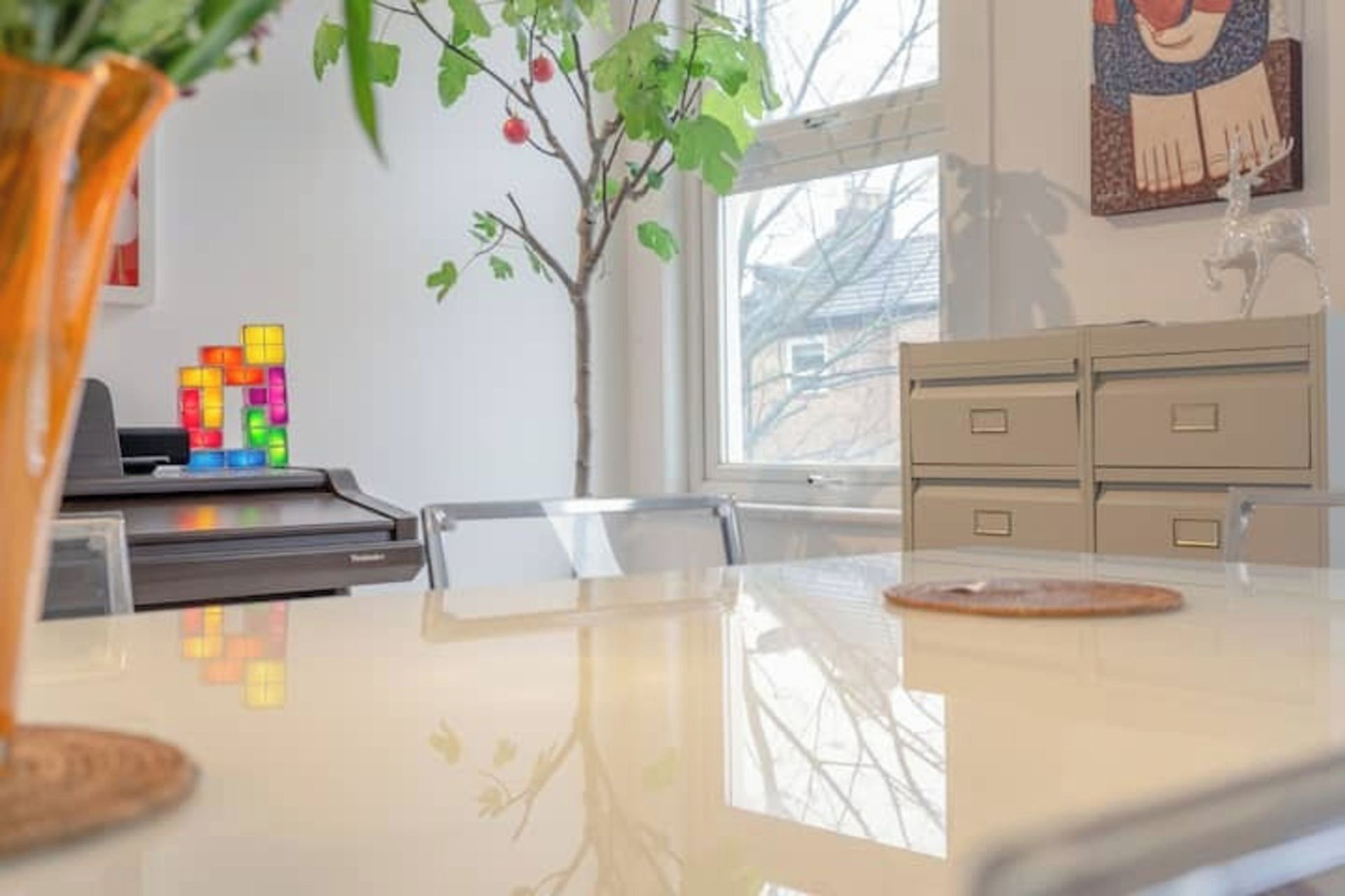 A room with a table, a plant, a window, and a desk with a computer.