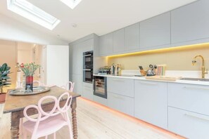A modern kitchen with grey cabinets, a wooden dining table, and a small potted plant. - Stylish & vast 2 bedroom apt in authentic London (London)