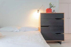 A bedroom with a bed, a dresser with drawers, a lamp, and a vase with flowers. - Stylish & vast 2 bedroom apt in authentic London (London)
