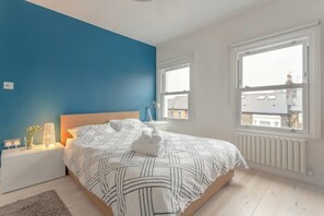 A bedroom with a bed, bedside tables, a nightstand, a window, and a view of buildings outside. - Stylish & vast 2 bedroom apt in authentic London (London)