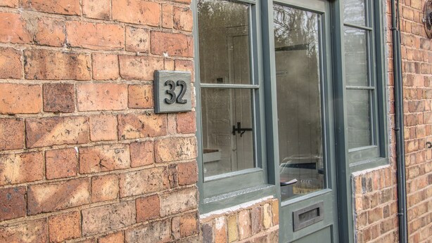 Un edificio de ladrillo con una ventana y una puerta, y un letrero con el número '32' en la pared.