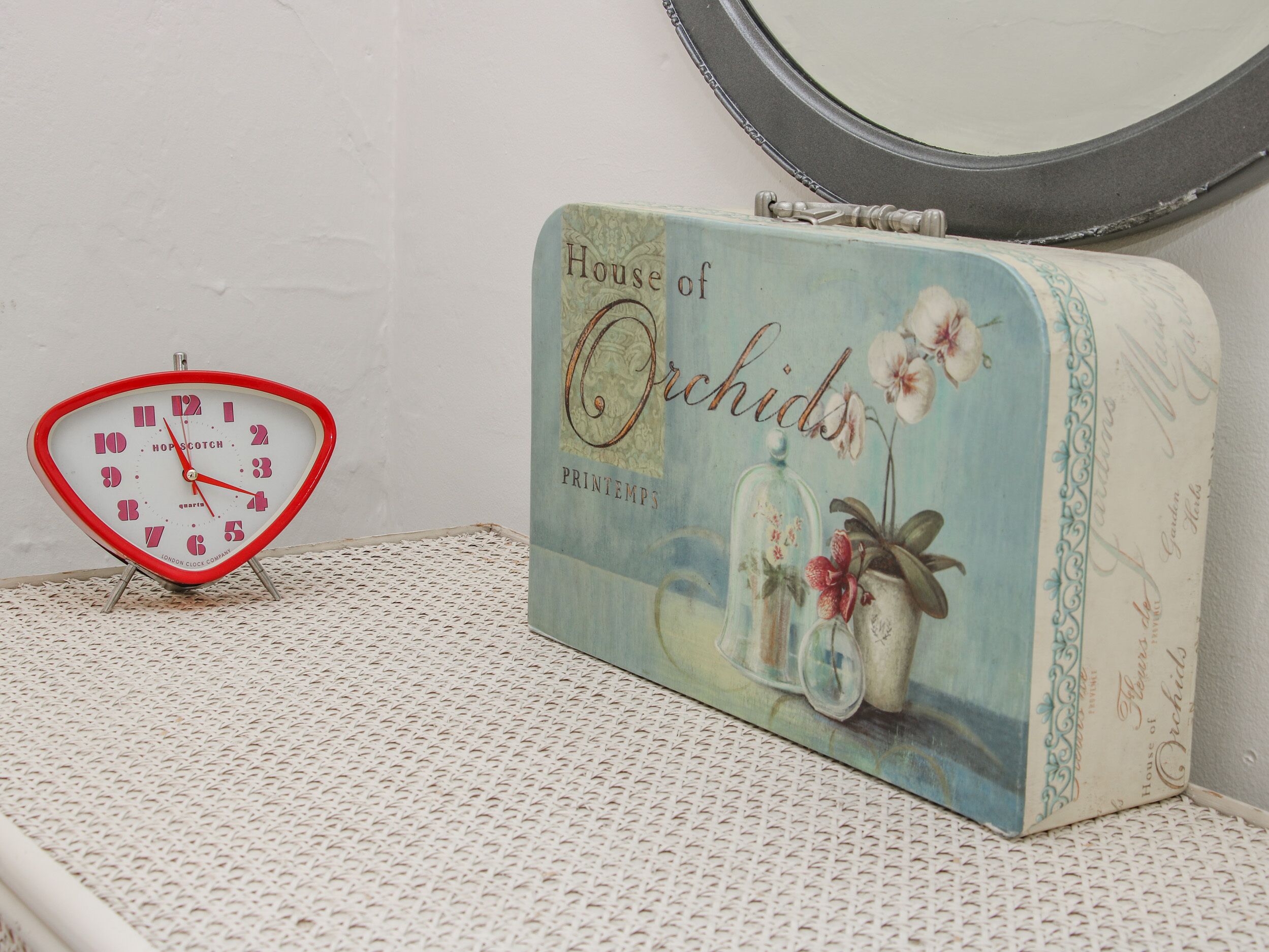 A vintage-style clock and a tin box labeled "House of Orchids" on a white shelf.
