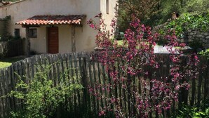 Un bâtiment rustique avec un toit en tuiles, entouré d’une clôture en bois et agrémenté de fleurs roses en pleine floraison.