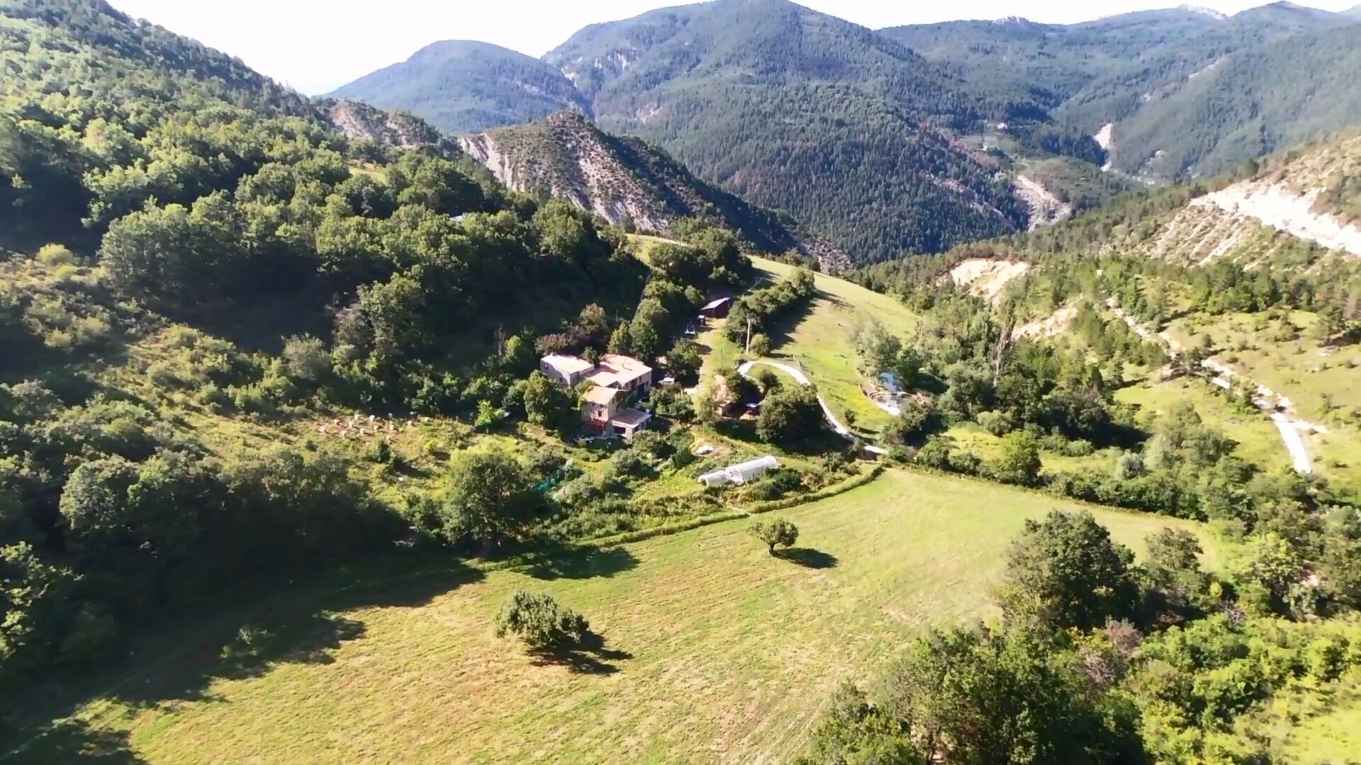 Un paisaje rural con un valle, casas dispersas y laderas boscosas.