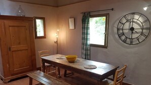 Un espace repas avec une table en bois, des bancs et des chaises. Une grande horloge murale est visible.