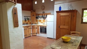 Une cuisine rustique avec des meubles en bois, une table à manger surmontée d’un saladier jaune et une fenêtre donnant sur un paysage verdoyant.