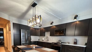 A modern kitchen with dark cabinetry, a stainless steel refrigerator, a dining table with chairs, and a colorful striped rug. - Jay Peak's Premier Ski-In / Ski-Out Location-just steps from the trail (Jay)