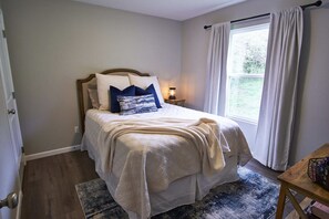 A bedroom with a bed, a nightstand, a window with curtains, and a door.