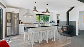 A modern kitchen with a central island, stainless steel appliances, pendant lighting, and a wood-burning stove. - Views on Parry - Lake Hāwea Holiday Home (Lake Hawea)