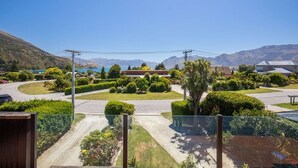 A residential area with a well-maintained lawn, a curved road, and a mountain backdrop. - Views on Parry - Lake Hāwea Holiday Home (Lake Hawea)