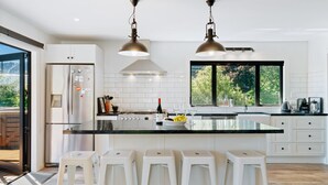 A modern kitchen with a large island, white cabinetry, stainless steel appliances, and two pendant lights. - Views on Parry - Lake Hāwea Holiday Home (Lake Hawea)