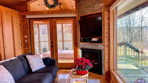 Interior acogedor de una cabaña de madera con chimenea, un sofá y un amplio ventanal con vistas al exterior.