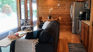 Interior acogedor de una cabaña con techo de madera, un sofá, una mesa de comedor y una zona de cocina.