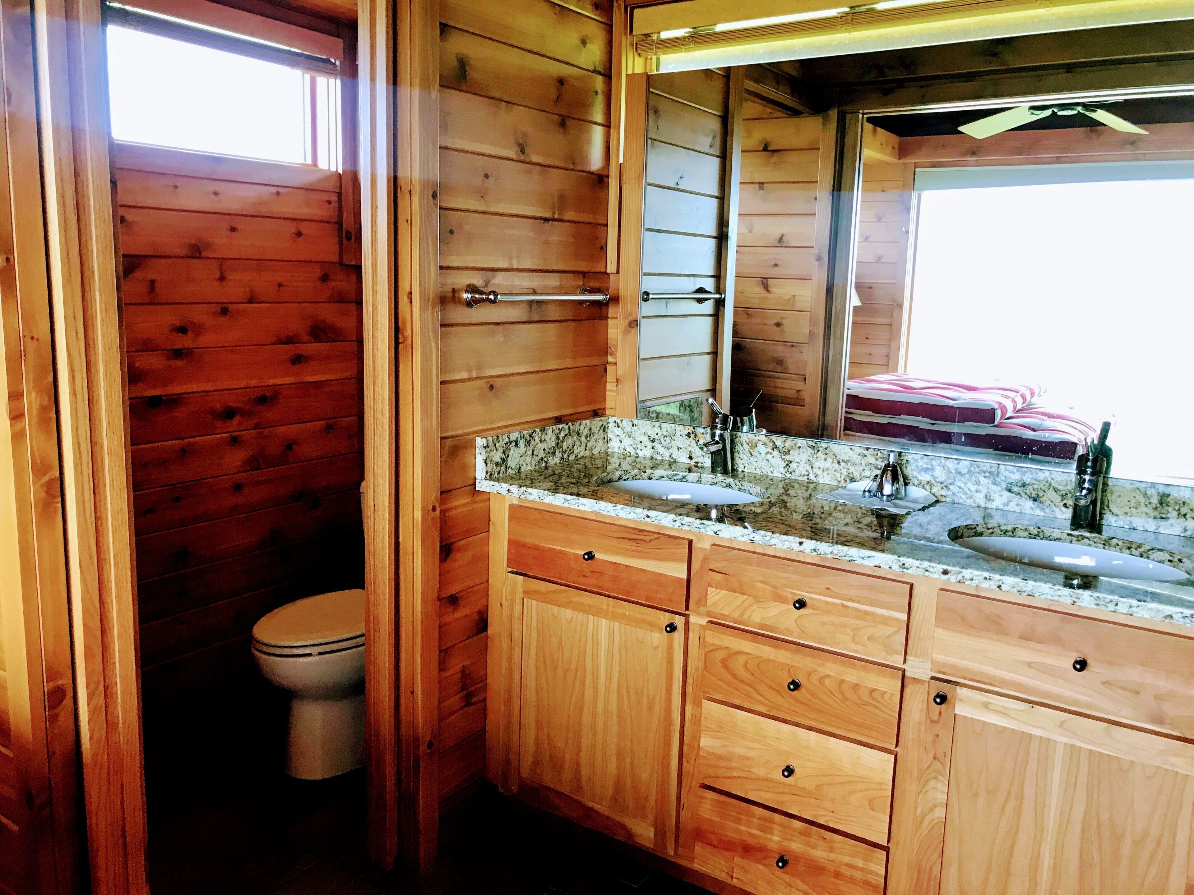 Une salle de bain rustique, aménagée dans une cabane en bois, avec des toilettes, un lavabo avec un miroir et des armoires en bois.