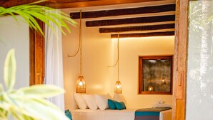 A room with a white sofa, a small table, and a painting on the wall. There is a wooden door frame with the number 4, and a plant in the foreground. - Café Jeri Hotel - Adults Only (Jijoca de Jericoacoara)