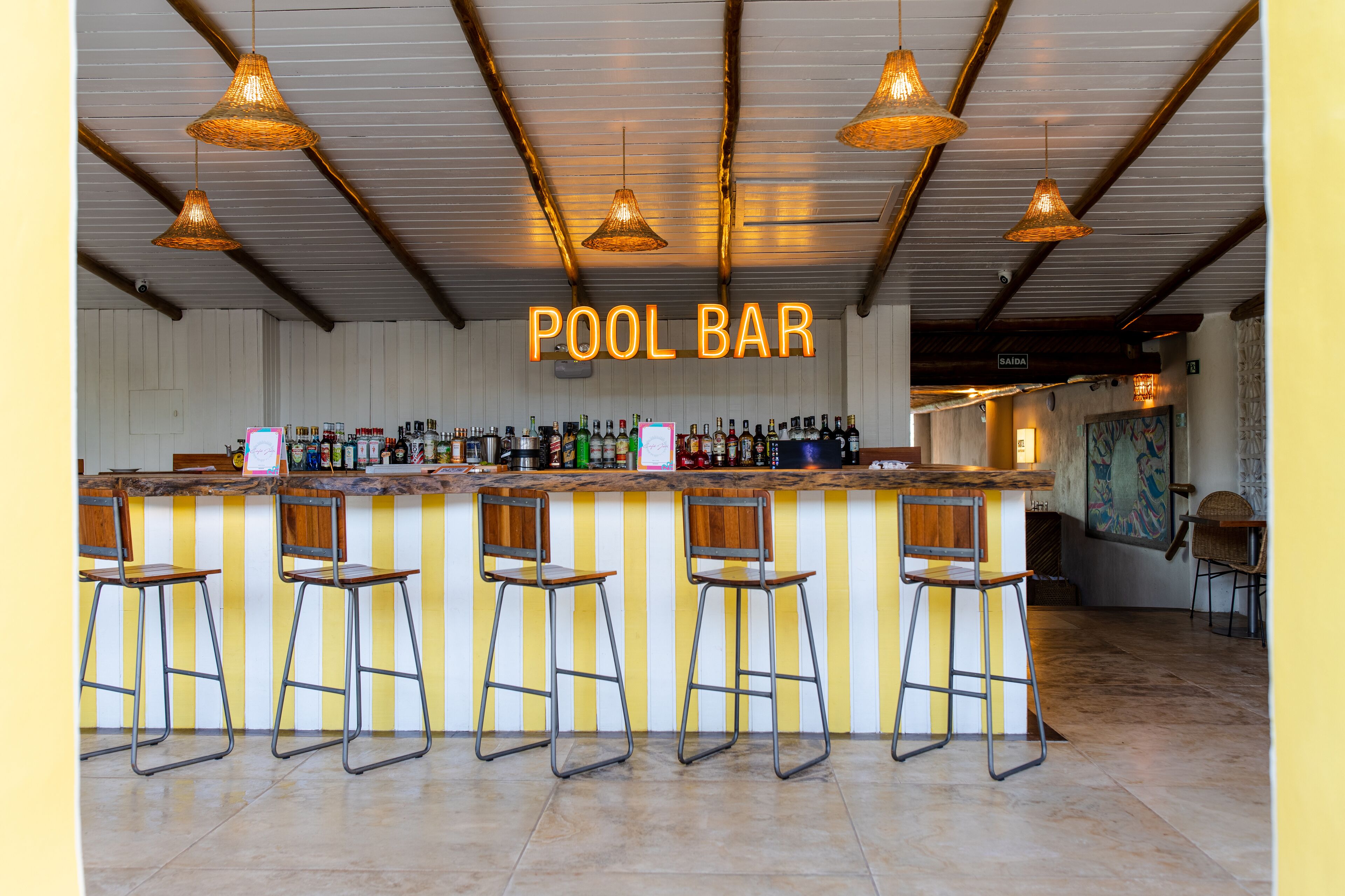 Eine Poolbar mit einer Holztheke, Metallhockern und hängenden Korbstühlen.