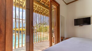A hotel room with a bed, a TV mounted on the wall, and a view of a pool area through a wooden door. - Café Jeri Hotel - Adults Only (Jijoca de Jericoacoara)