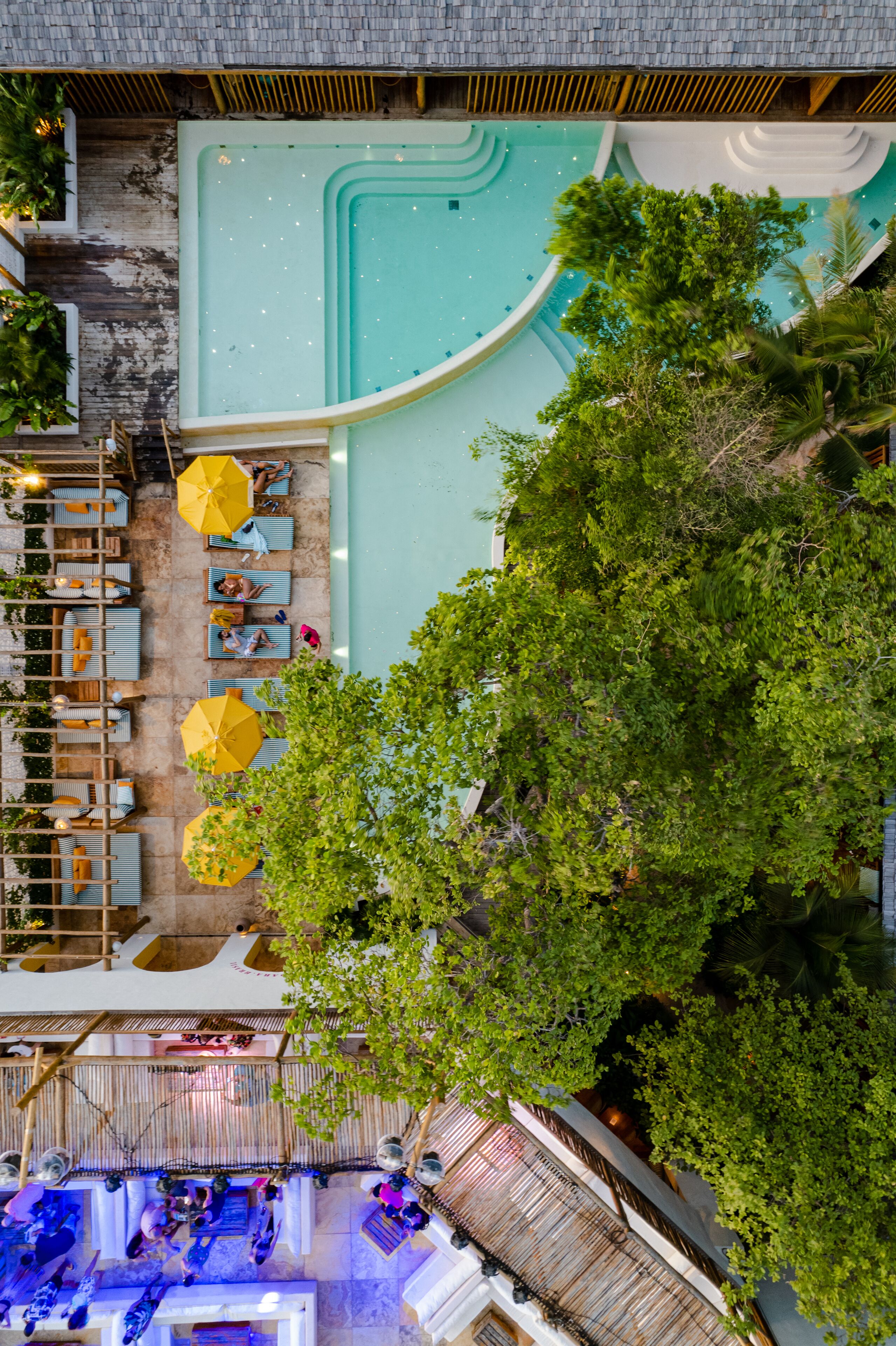 An aerial view of a rooftop pool area with multiple seating arrangements and umbrellas.