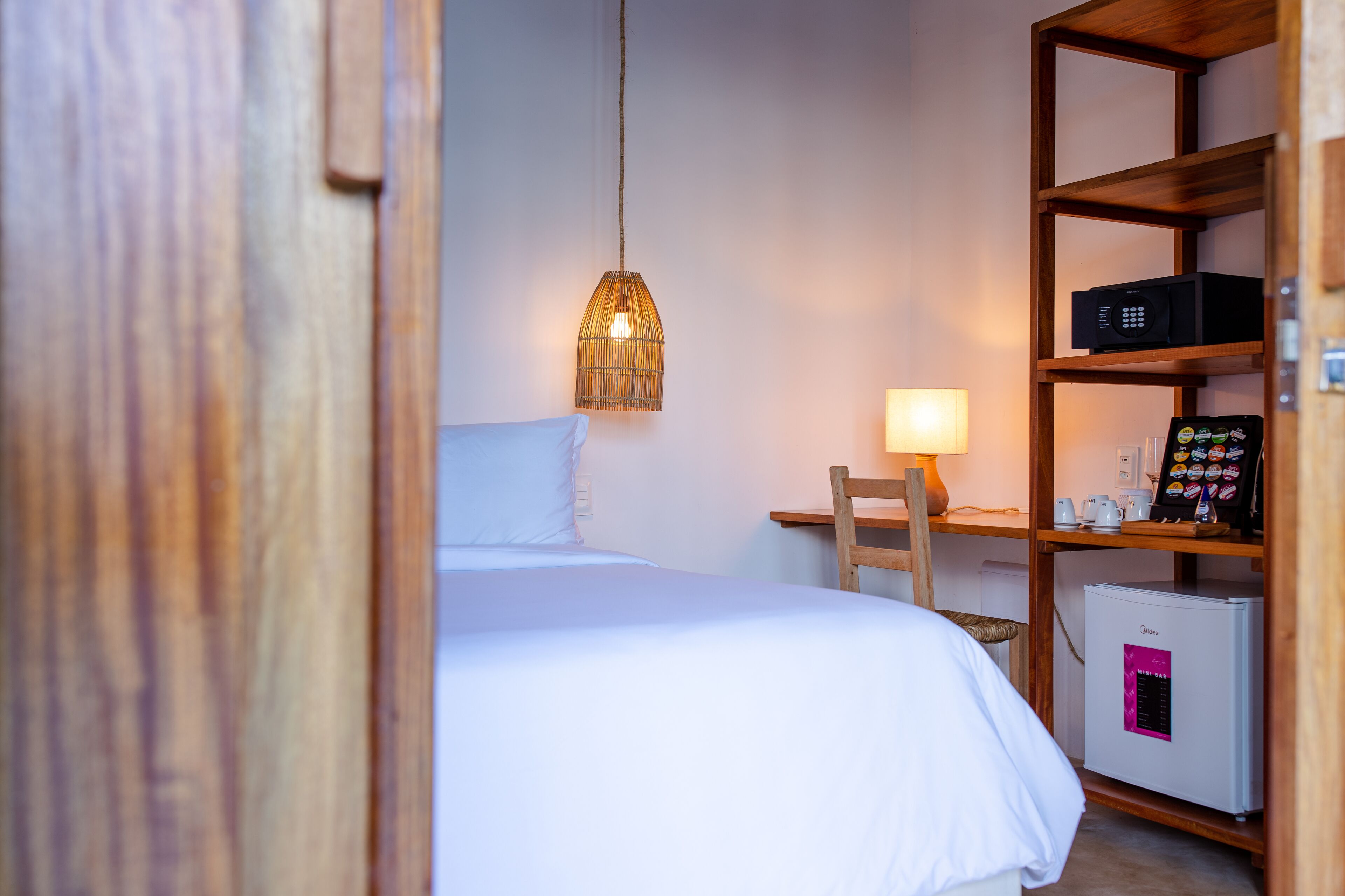 Ein Hotelzimmer mit einem Bett, einem kleinen Schreibtisch mit Lampe, einem Kühlschrank und einem Regal mit verschiedenen Gegenständen.