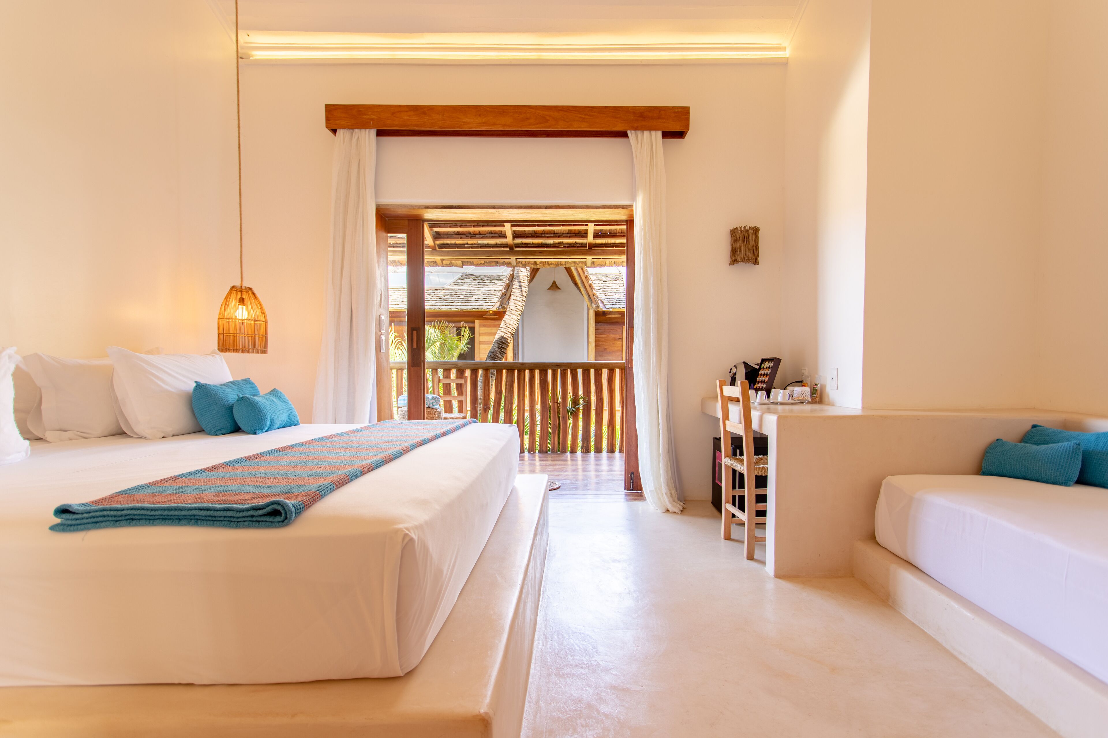 A room with a large bed, a smaller sofa, a desk, and a view through a wooden door.