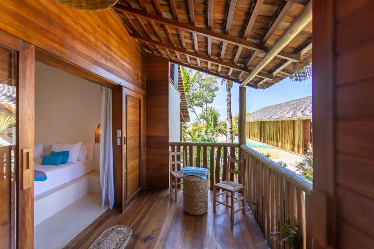 A wooden balcony with a bed, chairs, and a small table.
