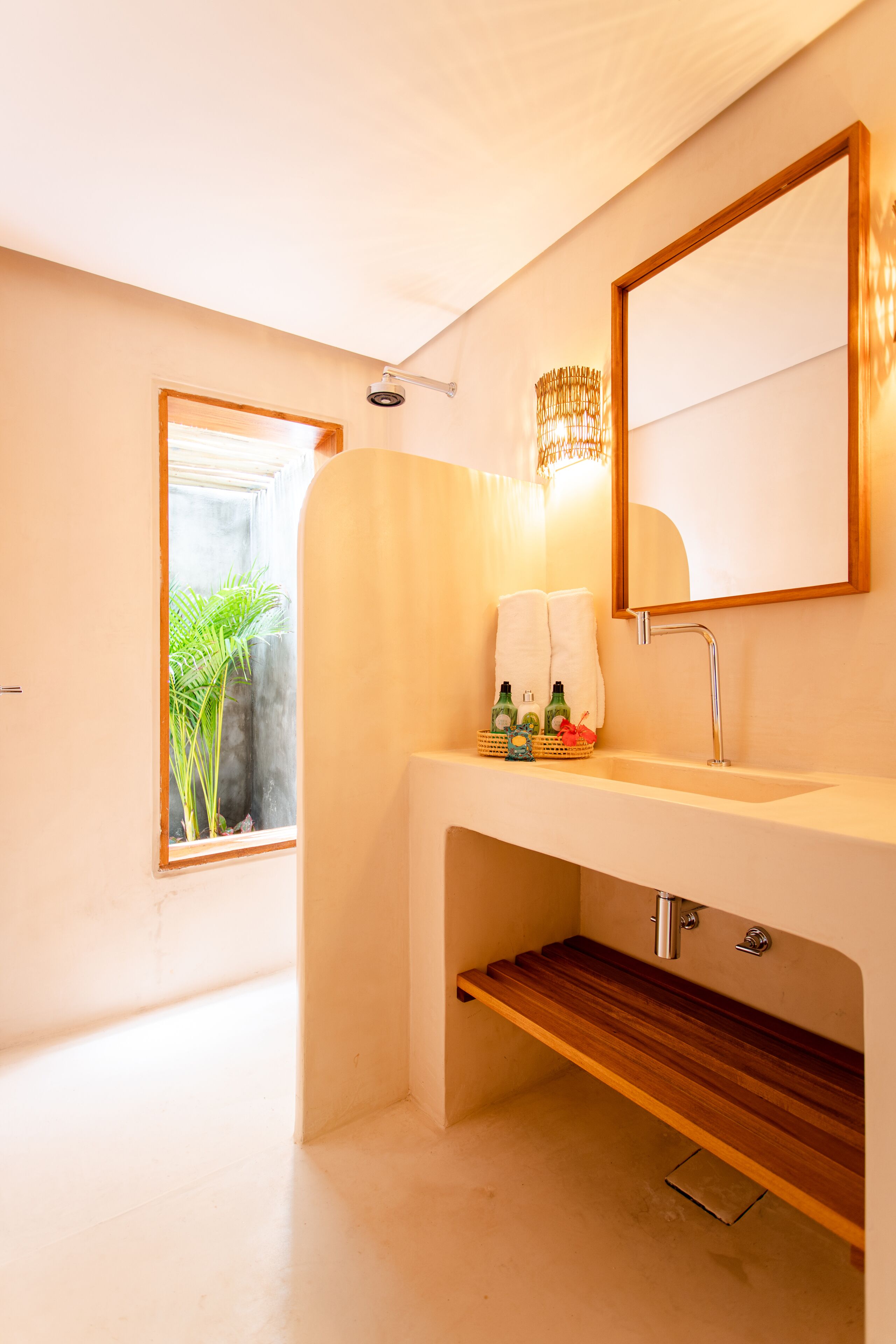 A modern bathroom with a large mirror, a sink, and a shower. There is a window with a view of greenery outside.