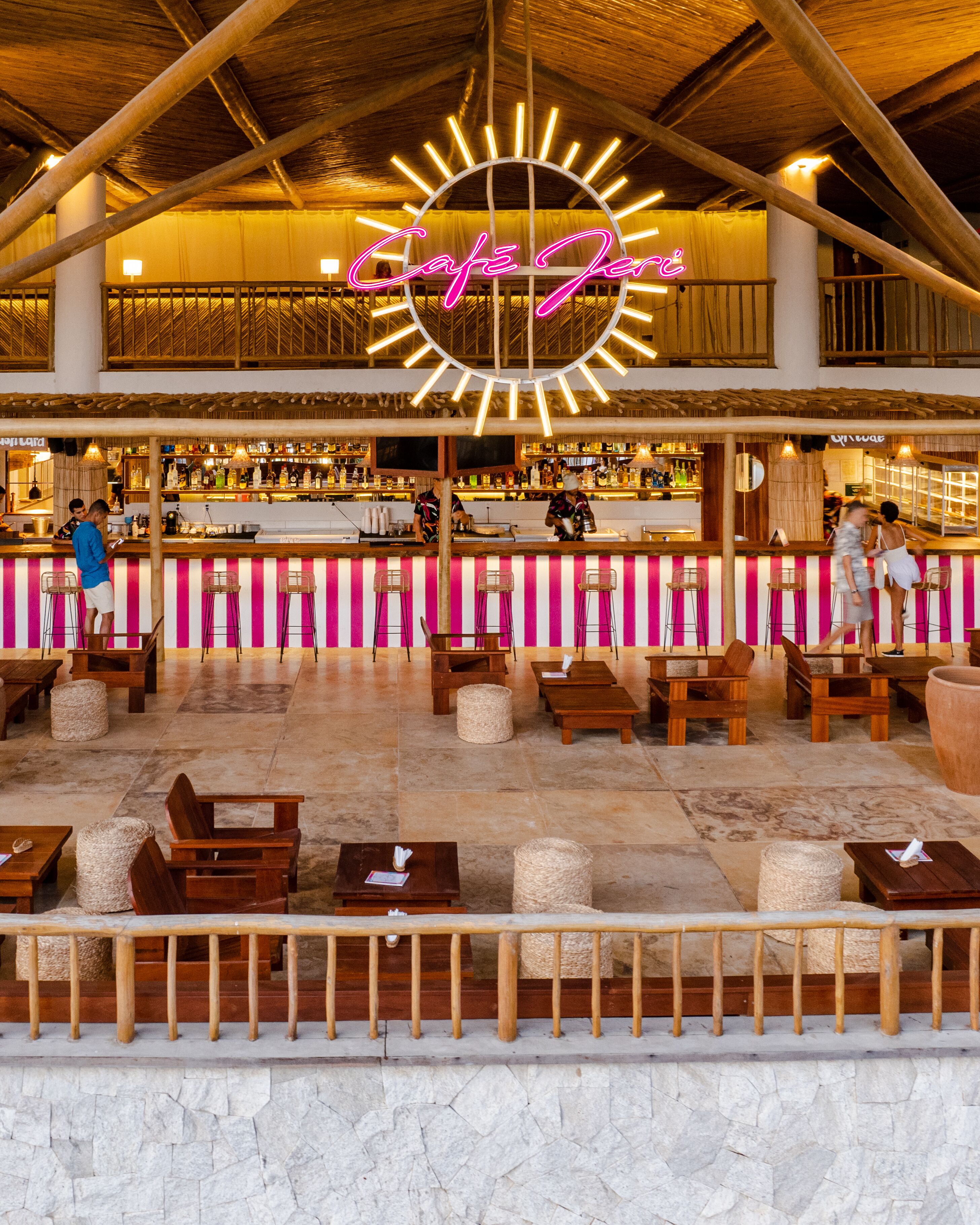 A bar area with a neon sign, wooden furniture, and a stone floor.