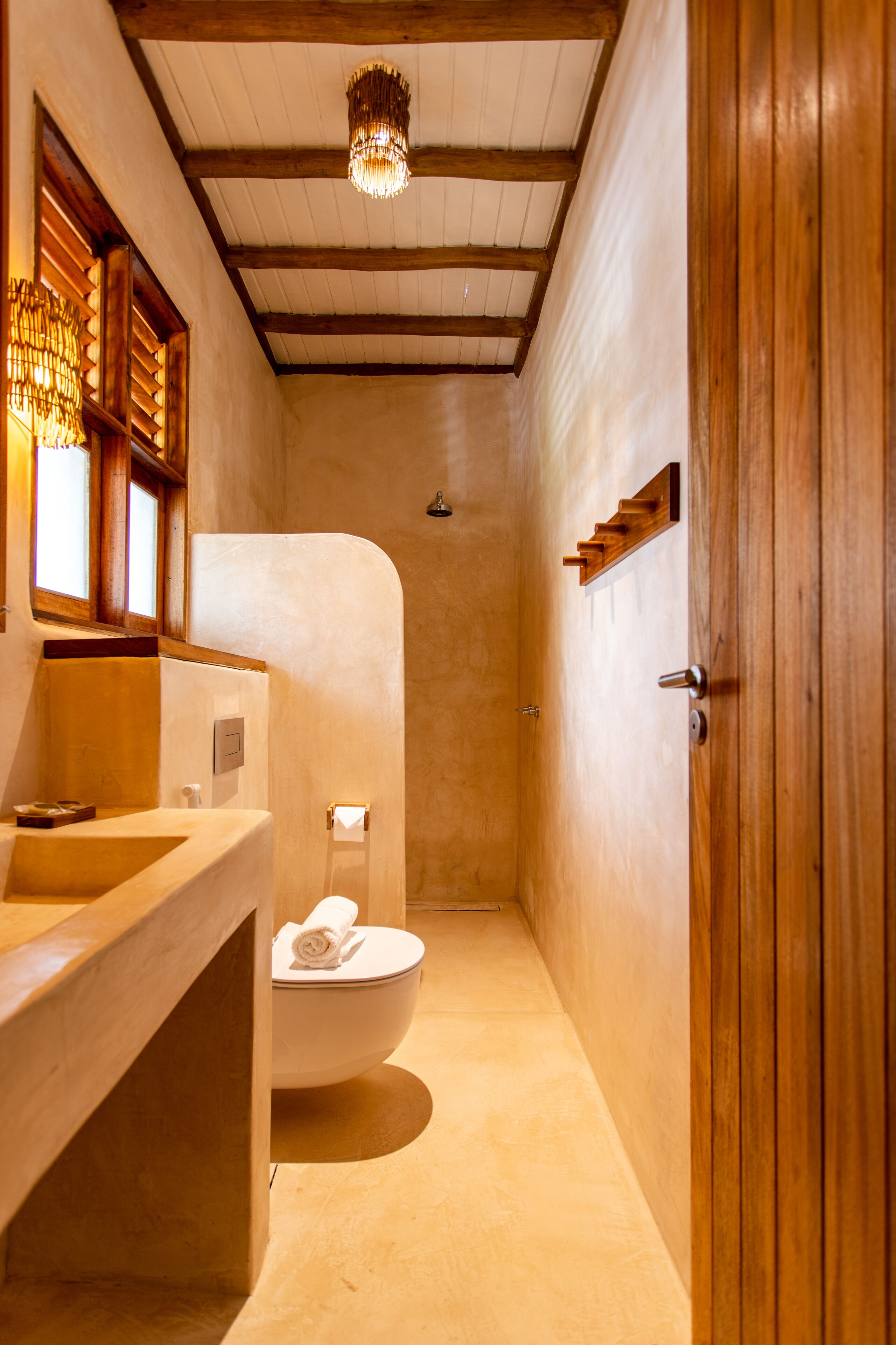 A narrow bathroom with a wooden vanity, a toilet, and a shower area.