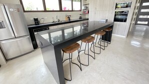 Een moderne keuken met een centraal eiland, barkrukken, roestvrijstalen apparatuur en een groot raam.