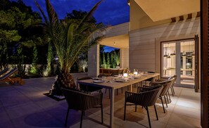 Un espace extérieur aménagé pour les repas, avec une table dressée pour six personnes, entourée de chaises, et une chaise de piscine en arrière-plan.